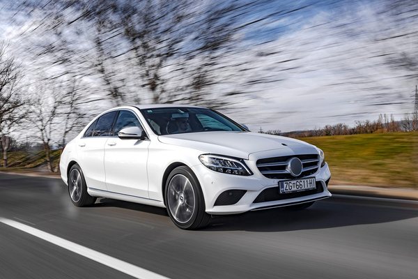 White sedan photographed in motion on a road, background blurred